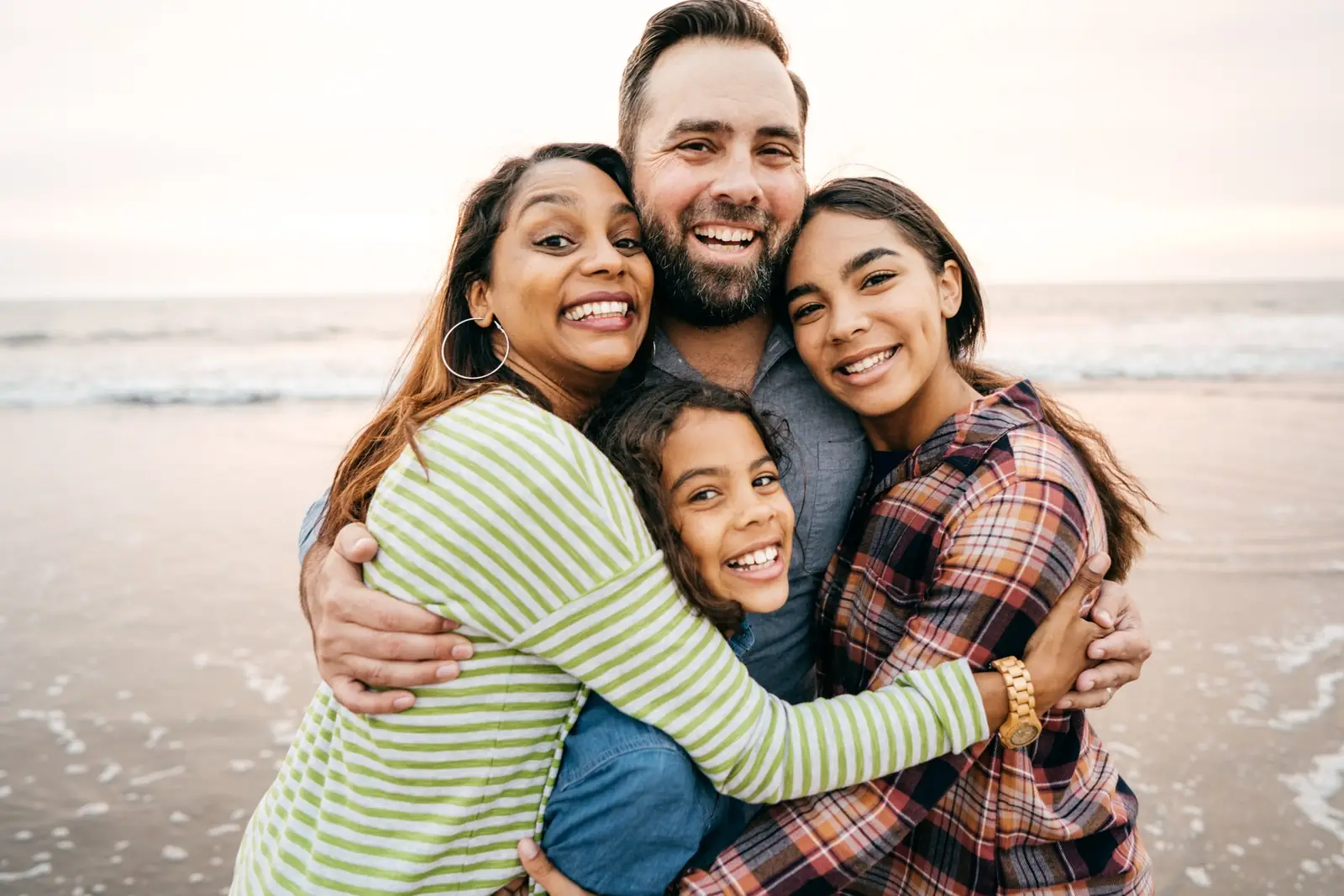 Two adults and two children smiling and embracing on a beach.
